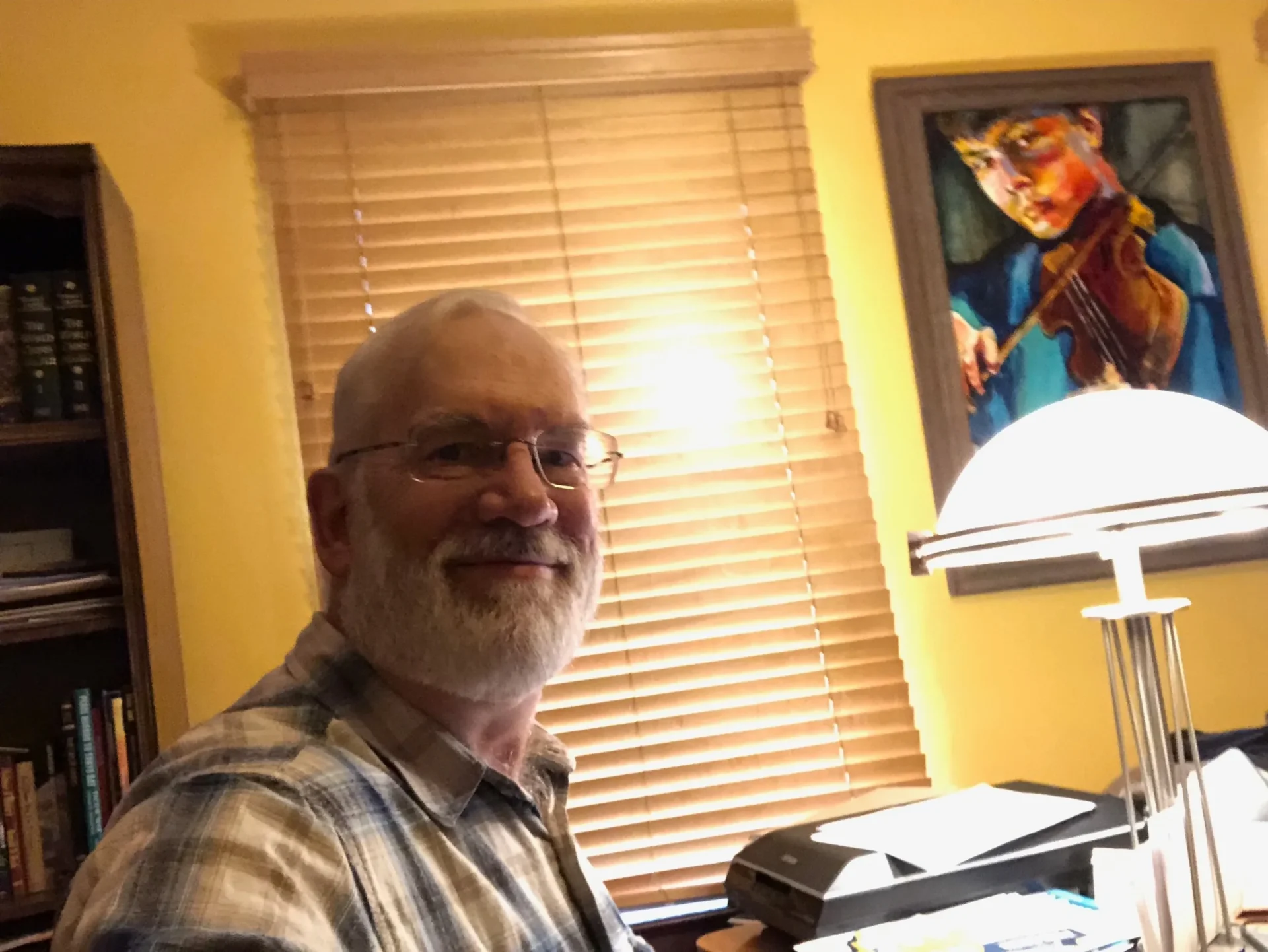 A man sitting in front of a window with a painting on the wall behind him.